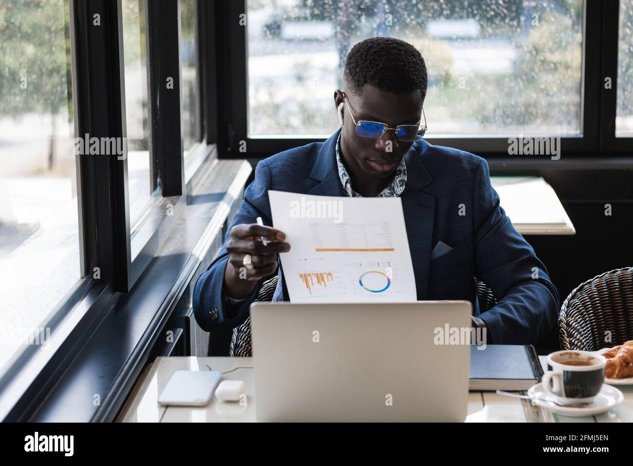Giovane imprenditore etnico maschile in occhiali con grafica su carta lavoro al tavolo del caffè Foto Stock