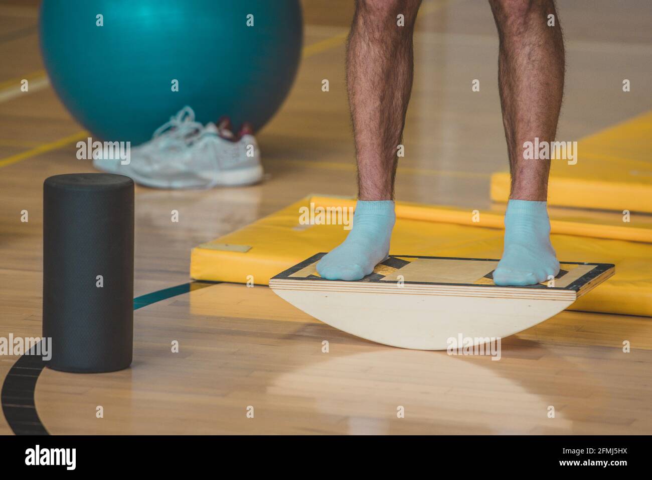 L'istruttore maschile ha visto usando una tavola di bilanciamento di legno. In una palestra al coperto si trovano diverse attrezzature sportive per l'equilibrio. Foto Stock