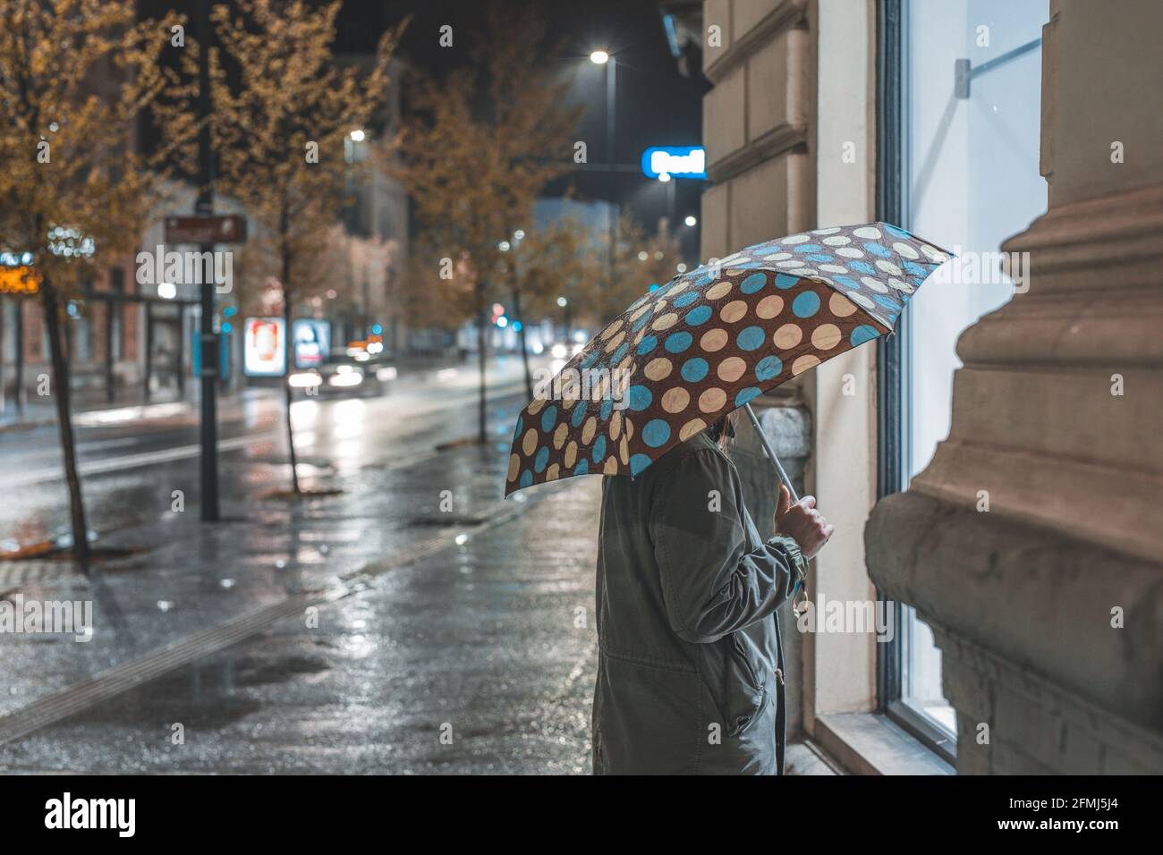 Sola donna che si prende il vento di notte durante la pioggia. Passeggiata piovosa attraverso la città. Foto Stock