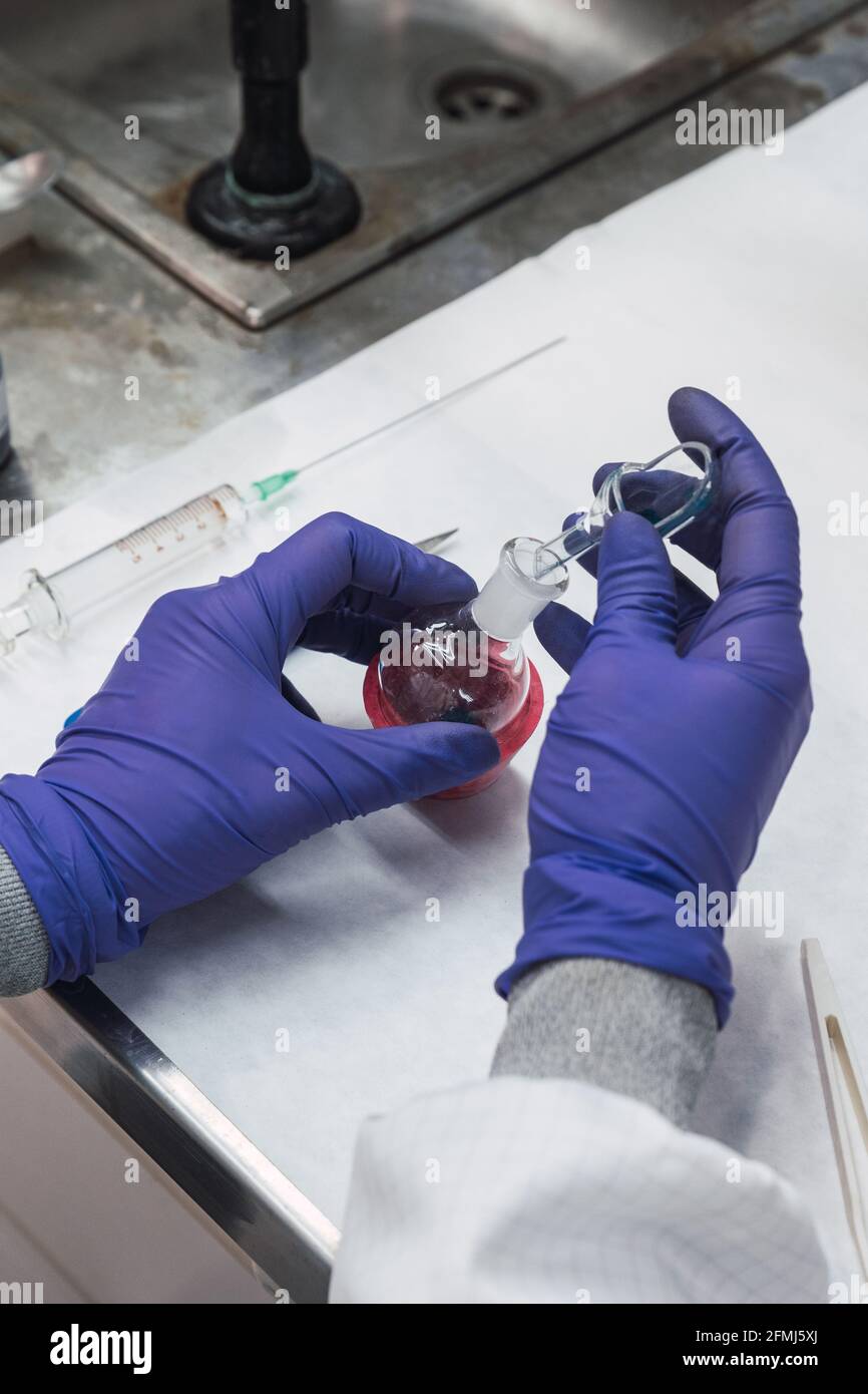 Da sopra raccolto chimico anonimo in guanti di lattice che riempiono vetro pipettare con liquido chimico dal pallone di ebollizione durante l'esecuzione del test in laboratorio Foto Stock