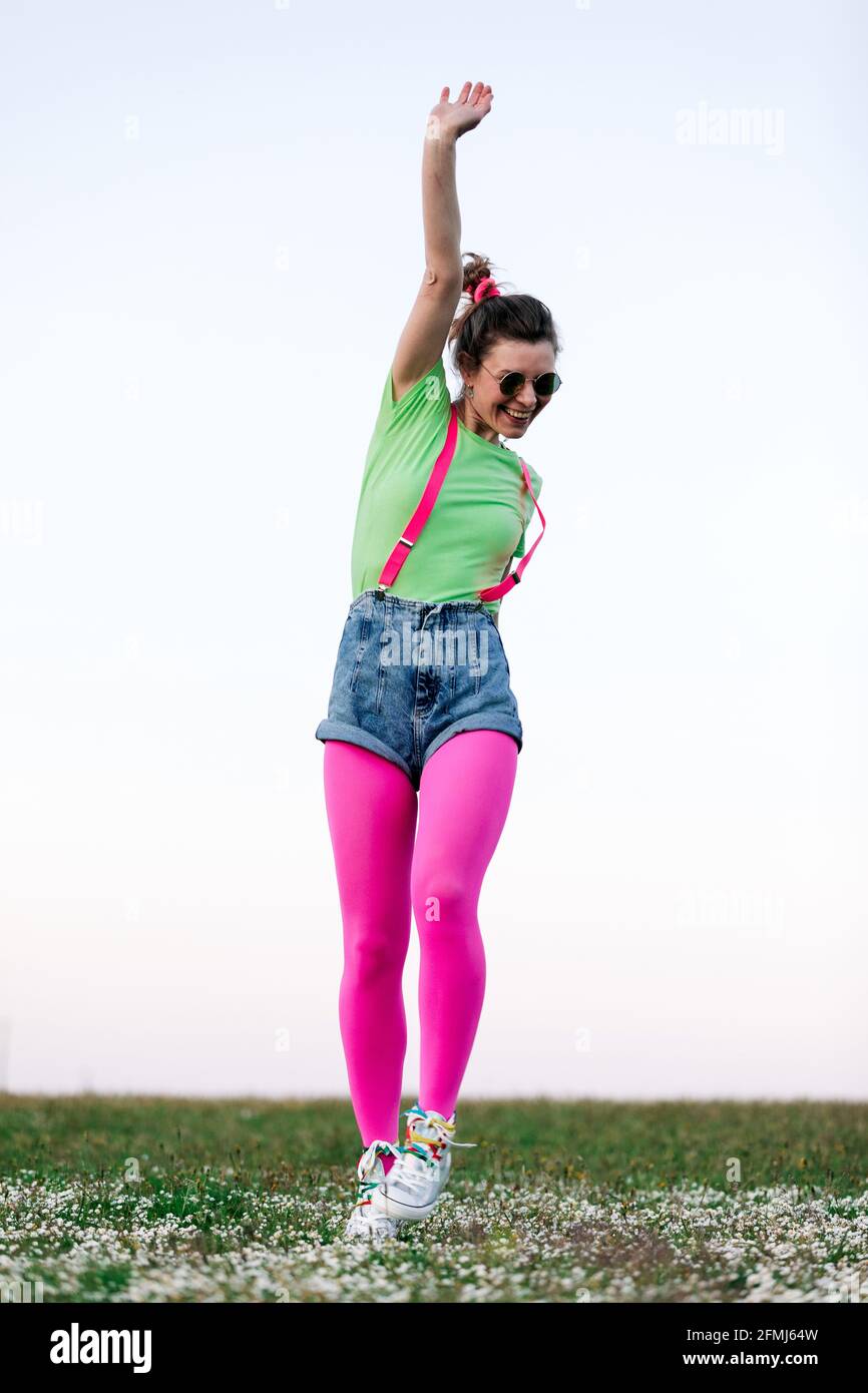 Calzoncini corti e rosa brillante per una giovane donna dal corpo pieno  collant che salta in maniera merrente con braccio sollevato su una  lussureggiante vetrata erbosa in natura Foto stock - Alamy