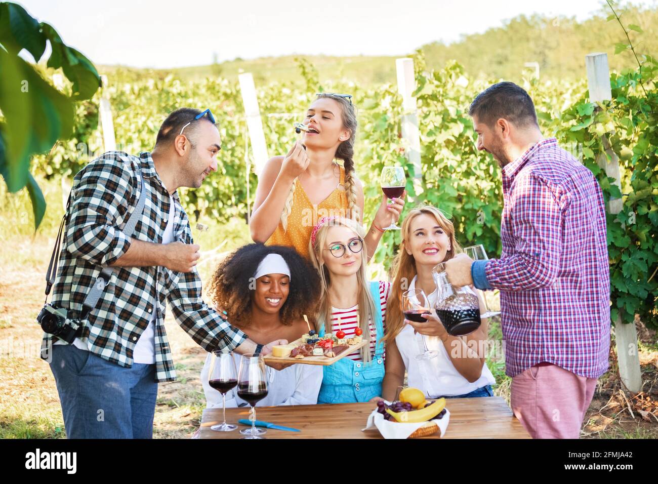 Felici amici multirazziali che si divertono insieme bevendo vino rosso e degustazione di bio-cibo in campagna vigneto Foto Stock