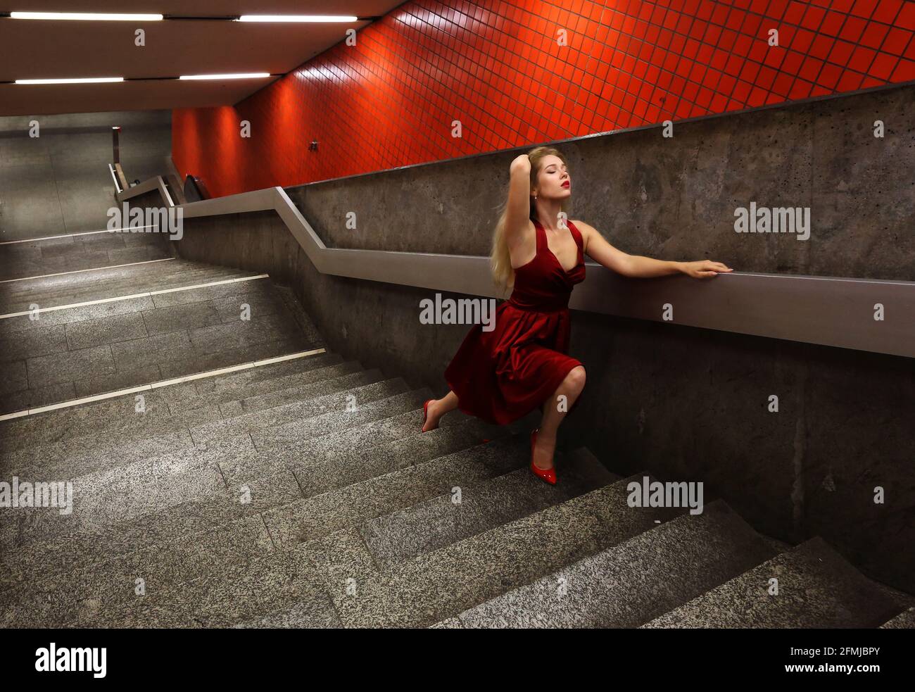 Nürnberg, U Bahn, Subway oder Metro a Nürnberg steht eine bionda junge Frau mit roten Kleid auf den Treppen zur Untergrundbahn Foto Stock