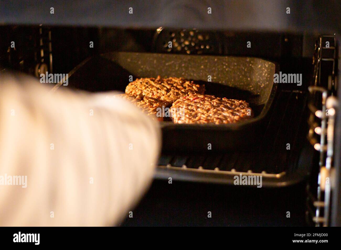 Mano mettendo hamburger carne macinata di manzo ad un forno. Processo di cottura hamburger a casa. Foto Stock