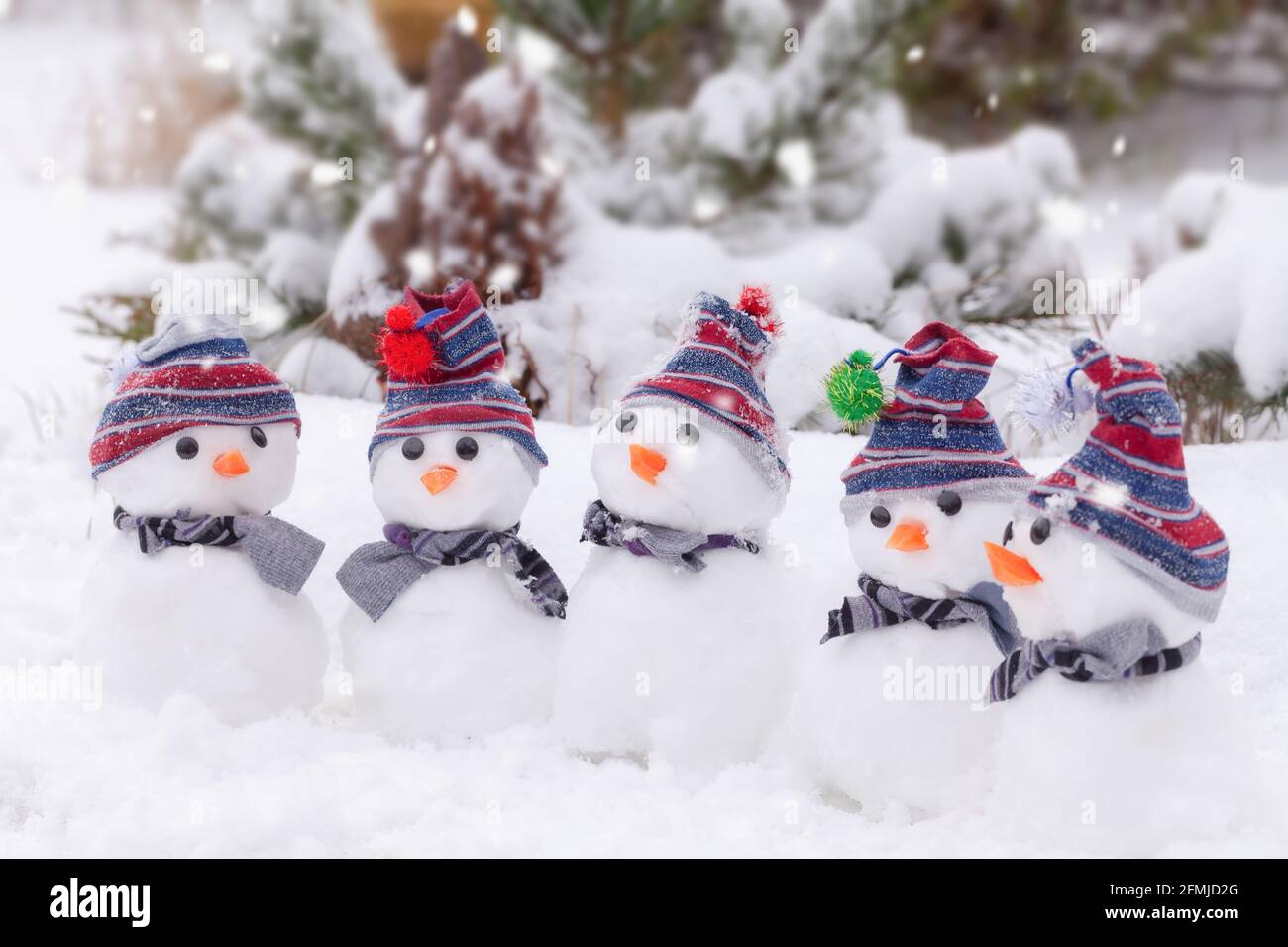 Simpatici pupazzi di neve con cappelli e sciarpe raggruppati in un paese delle meraviglie invernali di neve. Foto Stock
