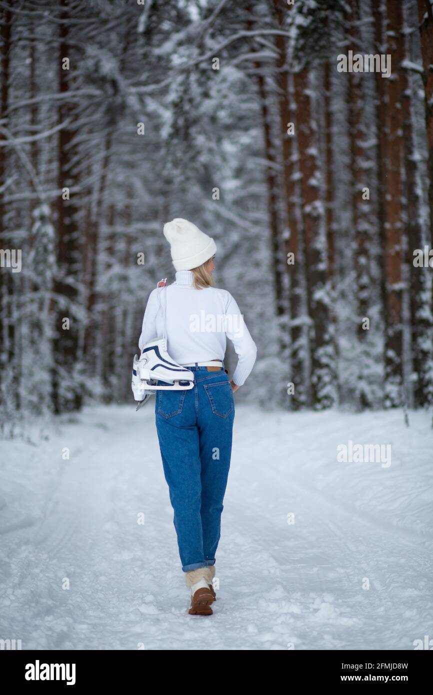 Giovane bionda bella femmina con pattini di ghiaccio bianco in mano nella foresta innevata invernale. Foto Stock