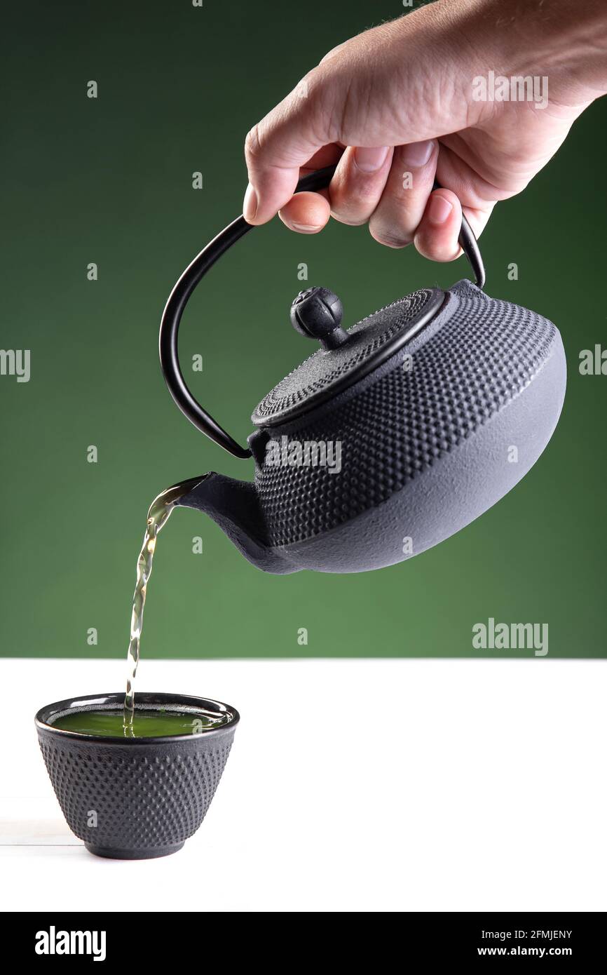 Acqua versata in una tazza scura di tè verde su sfondo verde con copia spazio.formato verticale. Foto Stock