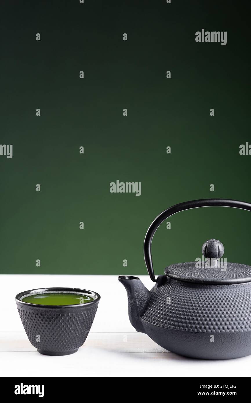 Tè verde e teiera su sfondo verde su base di legno bianco con copyspace. Bevanda tradizionale Giapponese. Formato verticale. Foto Stock