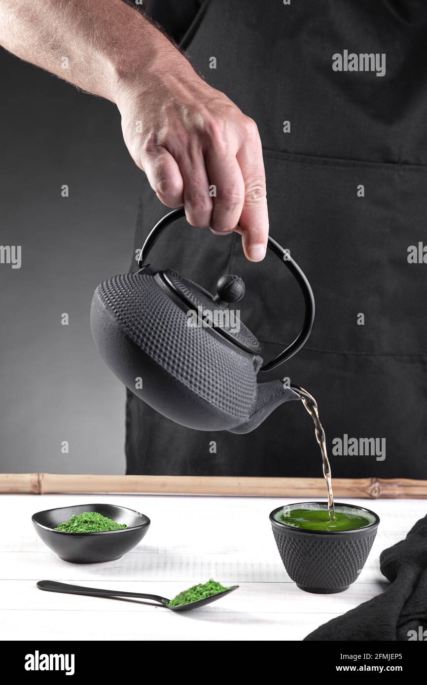 L'acqua è stata versata in una tazza scura di tè matcha su base bianca. Formato verticale. Foto Stock