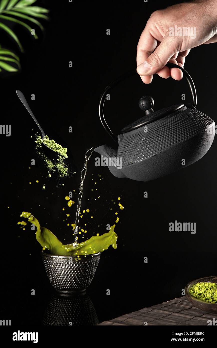 L'acqua è stata versata in una tazza scura di tè matcha su sfondo nero. Formato verticale. Foto Stock