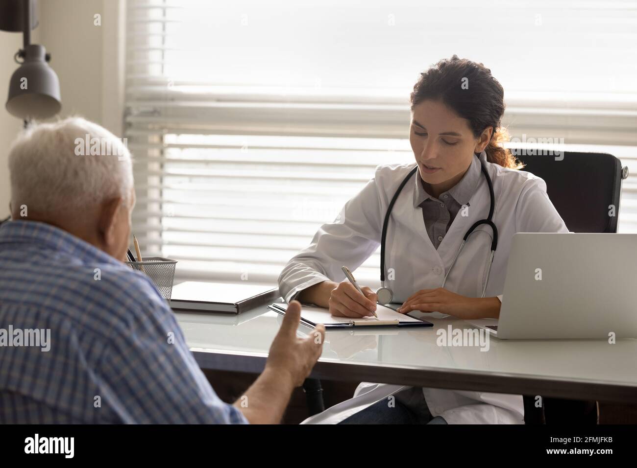 Attenta dottoressa che scrive anamnesi medica di pazienti anziani Foto Stock