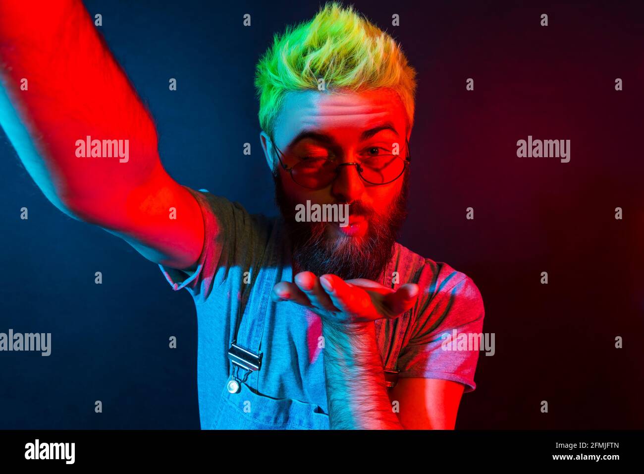 Romantico uomo hipster bearded con barba in tute in denim che parla via web camera con la fidanzata, esprimendo l'amore, trasmettendo in diretta streaming. Colorato Foto Stock