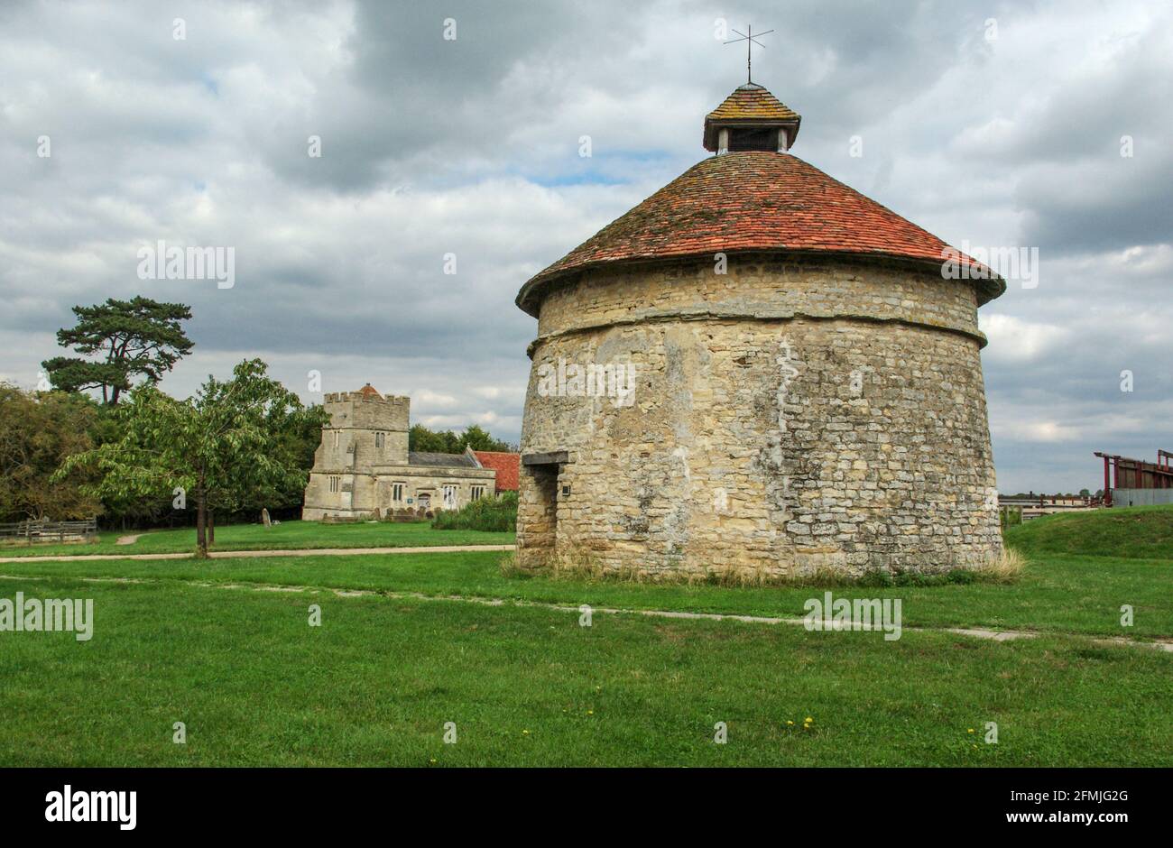 Colombaia medievale nel villaggio desertato di Furtho, Northamptonshire, Inghilterra, UK; chiesa di San Bartolomeo sullo sfondo. Foto Stock