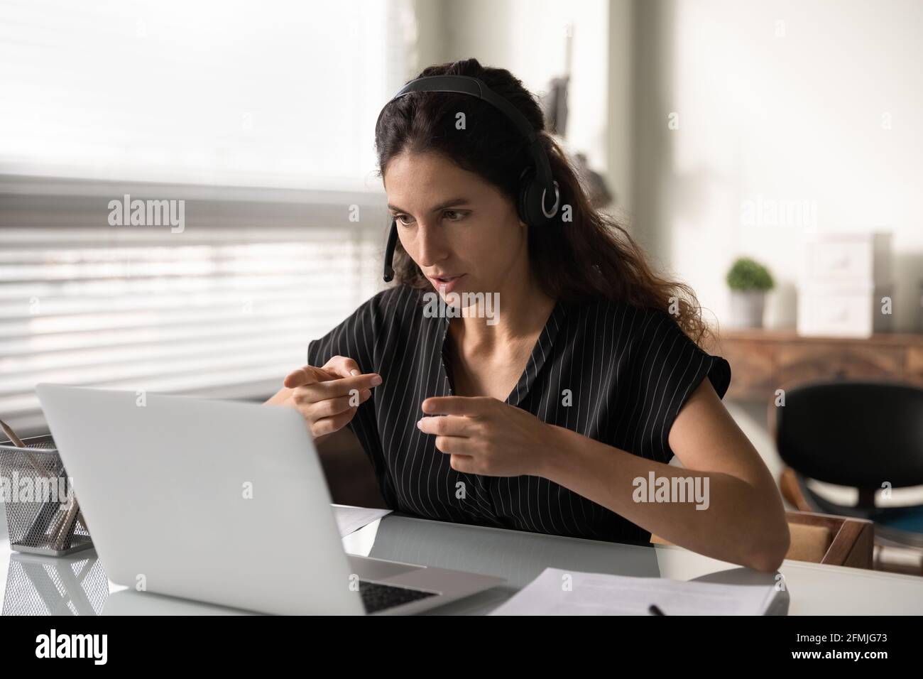 La donna concentrata in cuffia siede dal client di supporto del pc in remoto Foto Stock