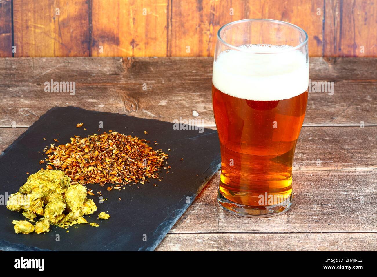 Bicchiere da pinta riempito con birra sul lato di a. ardesia ripiena di luppolo e di malto d'orzo da birra Foto Stock