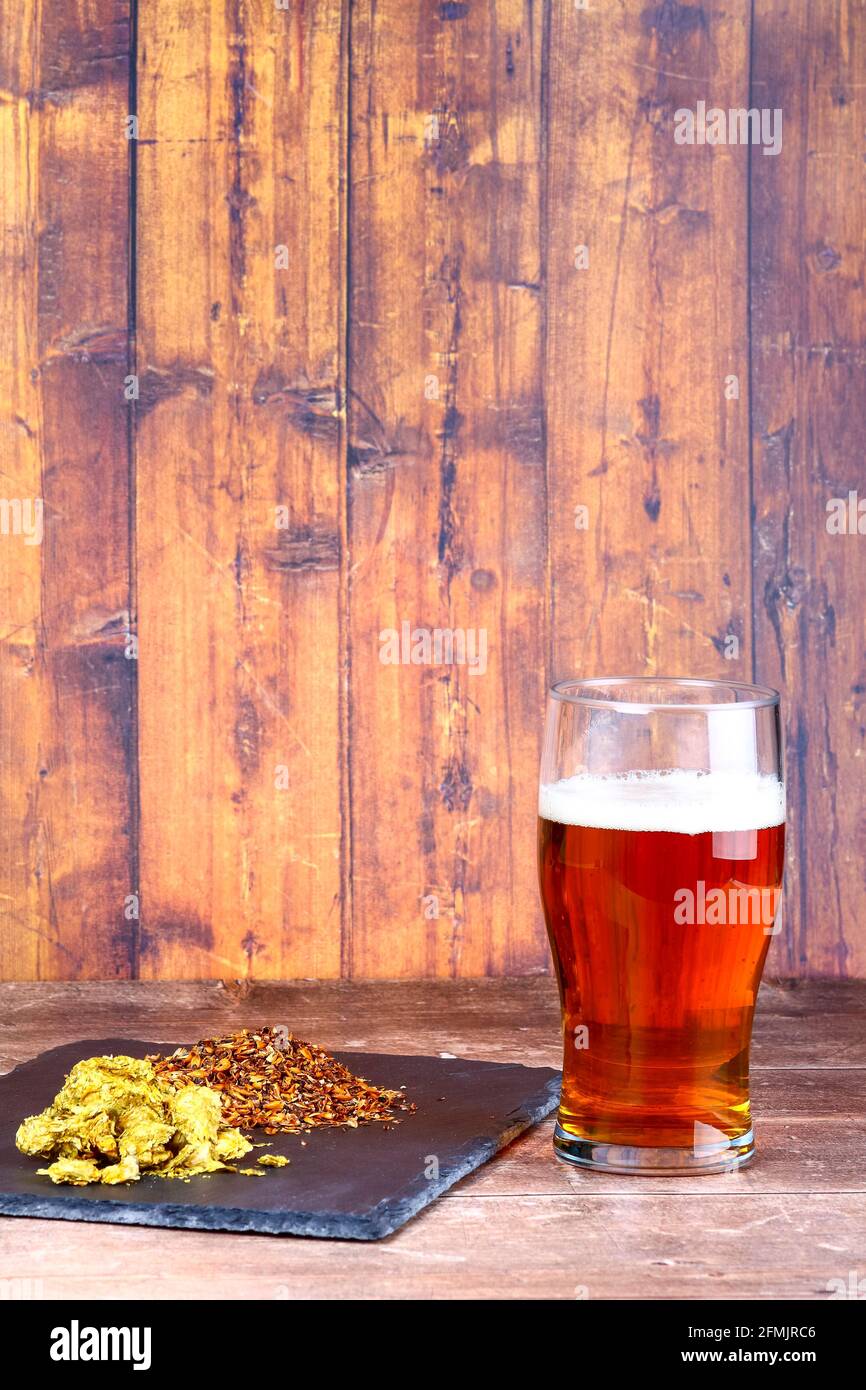 Bicchiere da pinta riempito con birra sul lato di a. ardesia ripiena di luppolo e di malto d'orzo da birra Foto Stock
