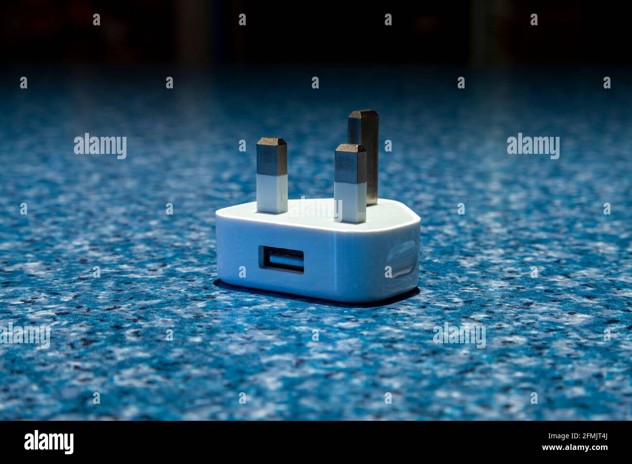 Una spina a 3 pin sul retro con un connettore usb per ricaricare i telefoni su una superficie blu a chiazze. Northampton, Inghilterra, Regno Unito. Foto Stock