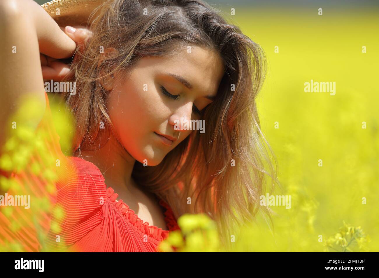 Ritratto di una donna di bellezza in rosso che posa in una campo fiorito giallo Foto Stock