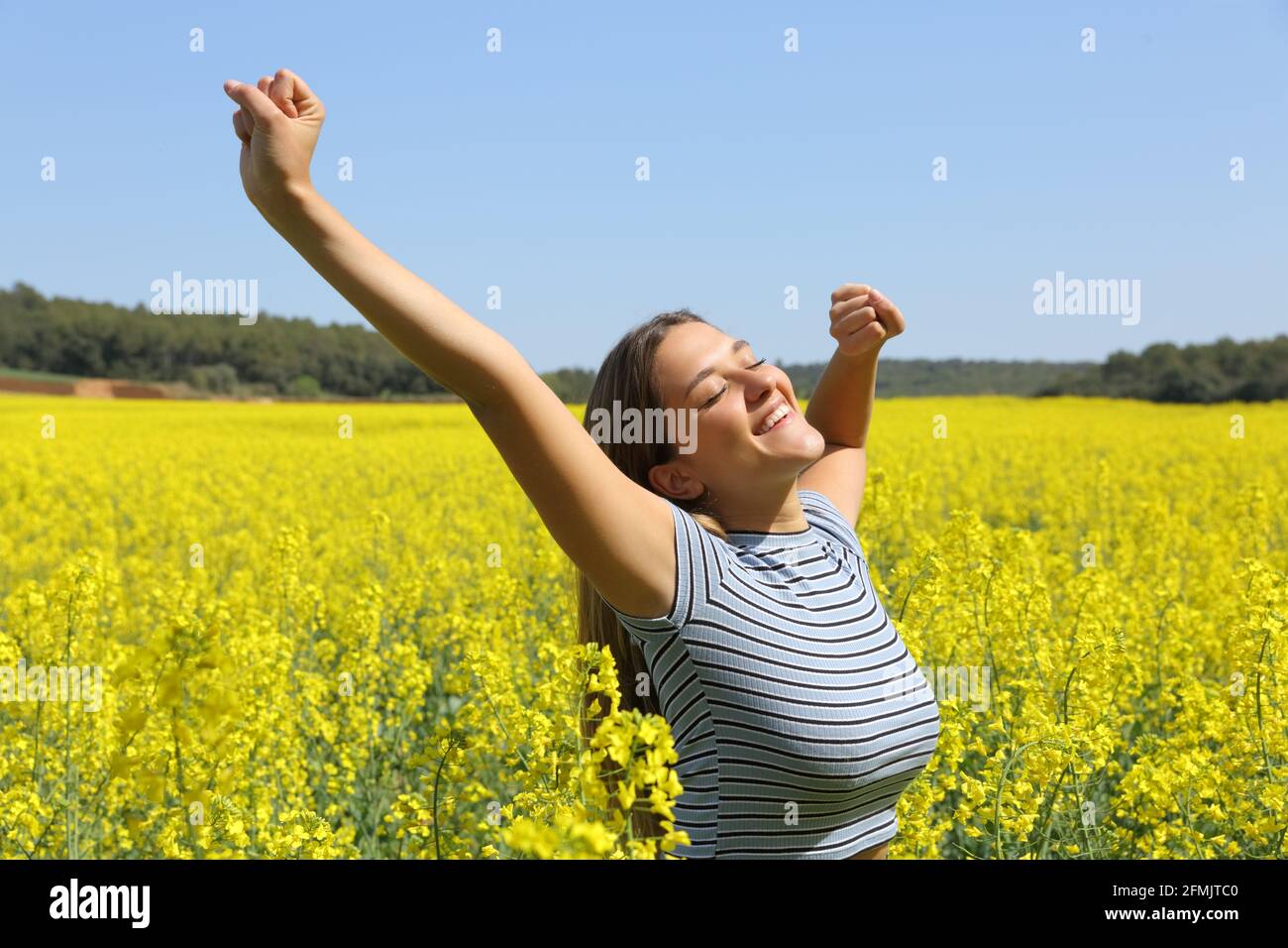 Donna felice che allunga le braccia in un campo fiorito giallo dentro stagione primaverile Foto Stock