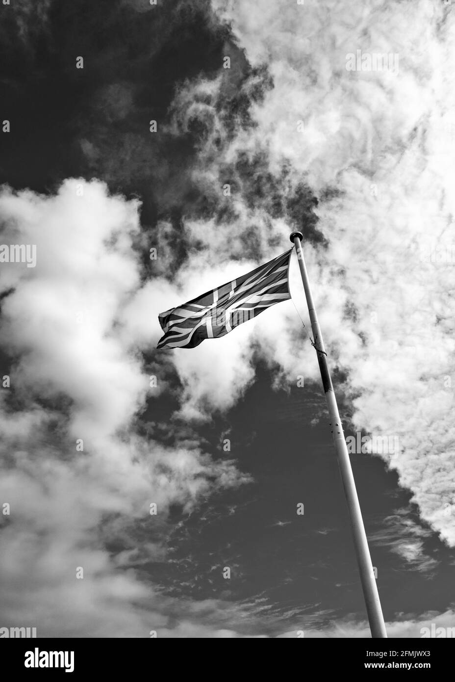 La bandiera dell'Unione britannica (Union Jack) su un palo di bandiera contro un cielo blu con soffici nuvole bianche. Fotografia in bianco e nero. Foto Stock