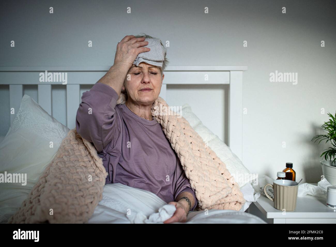 Donna anziana malata con mal di testa a letto a casa, mal di testa ed effetti collaterali degli effetti vaccinali. Foto Stock