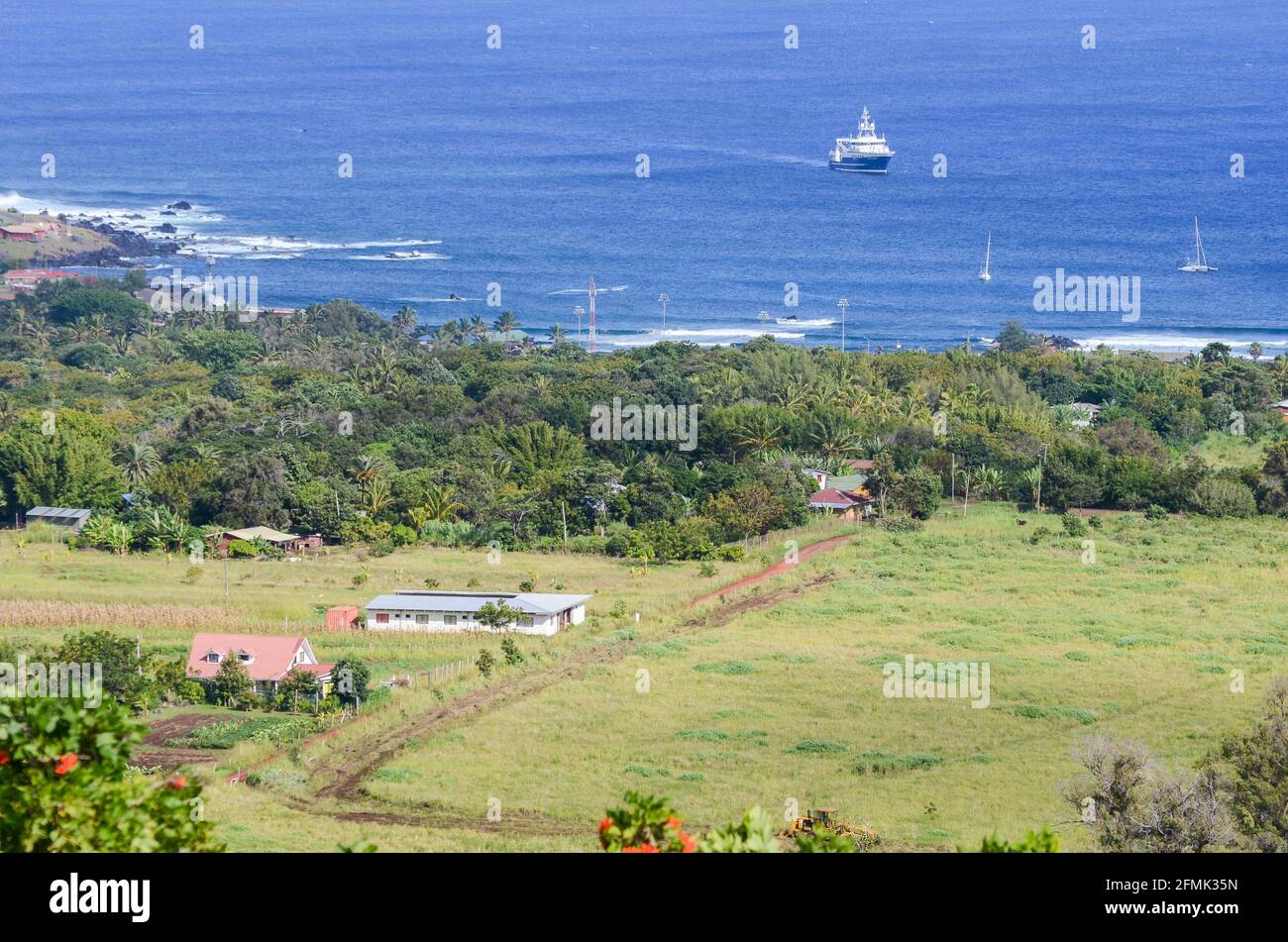Vista di una fattoria con un campo piantato alla periferia di Hanga Roa, Isola di Pasqua, Cile. Una nave ancorata al largo della costa può essere vista sullo sfondo. Foto Stock