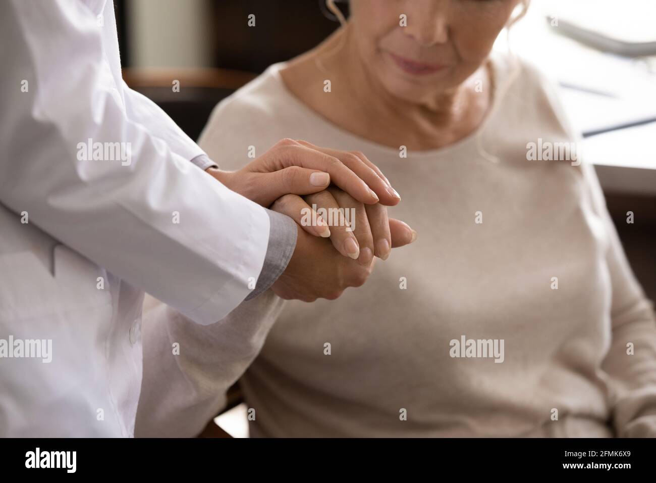 Mano femminile anziana disabile nei palmi della giovane donna medic Foto Stock