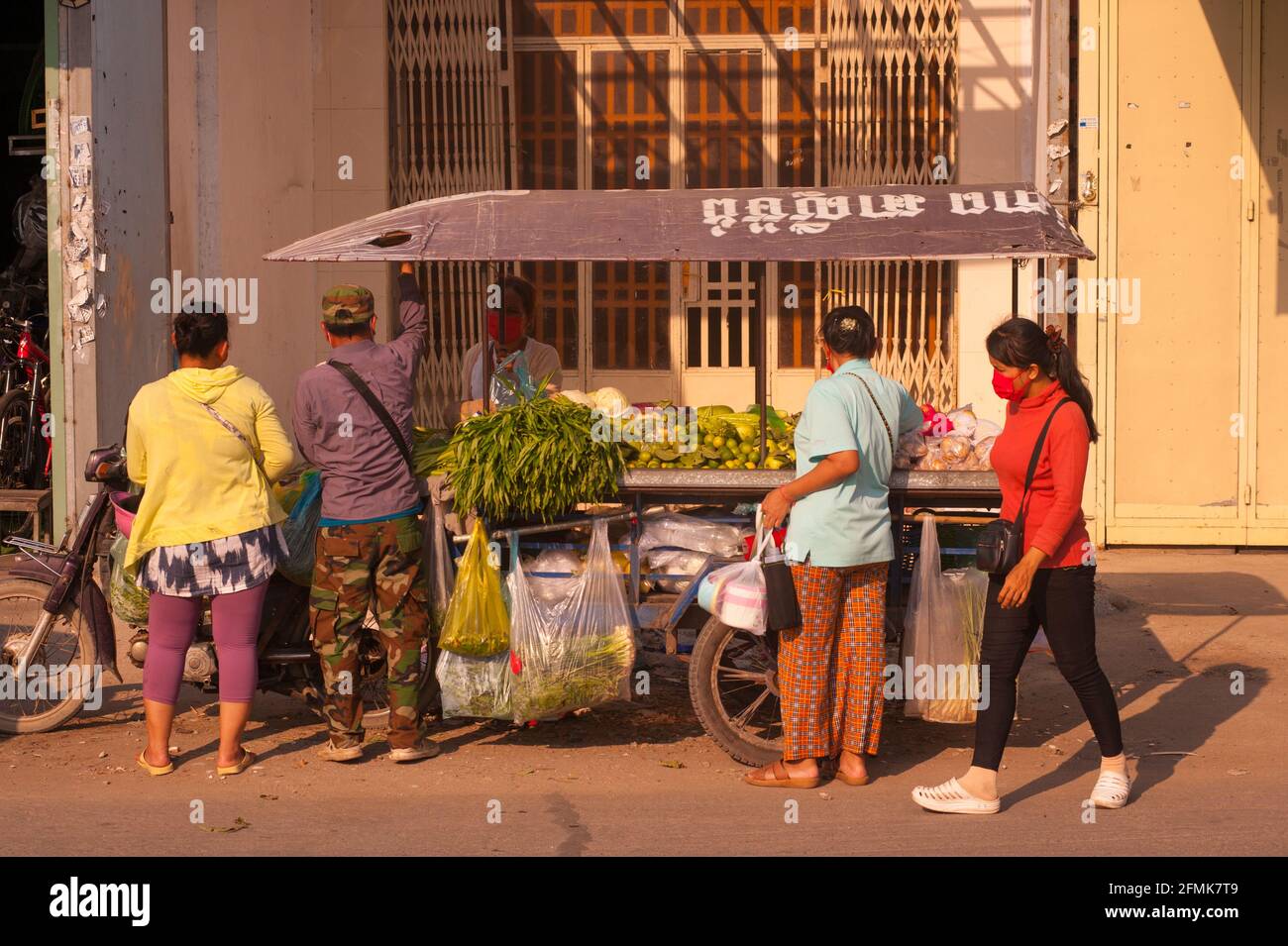 Phnom Penh, Cambogia. 10 maggio 2021. Dopo 3 settimane di totale isolamento della città, il governo ha diviso Phnom Penh in 3 zone di colore (rosso, arancione e giallo) a causa dell'ondata di COVID-19 in corso. Un carrello di verdure mobile si posiziona in una zona rossa, il che significa un alto rischio di infezione. I cambogiani, che si divertono con la loro zona di colore, si vestono in rosso e indossano maschere rosse. Crediti: Kraig Lieb / Alamy Live News Foto Stock
