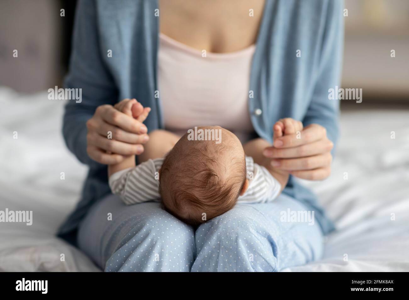 Cura della madre. Unriconoscibile mummia legame con il suo bambino a casa, tenendo il bambino neonato su giri, lulling lui a dormire mentre si siede sul letto in essere Foto Stock