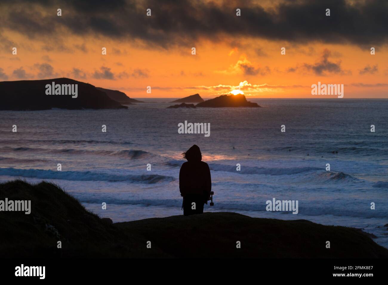 Una persona in piedi sulla costa silhouette da un intenso tramonto a Fistral Bay a Newquay in Cornovaglia. Foto Stock