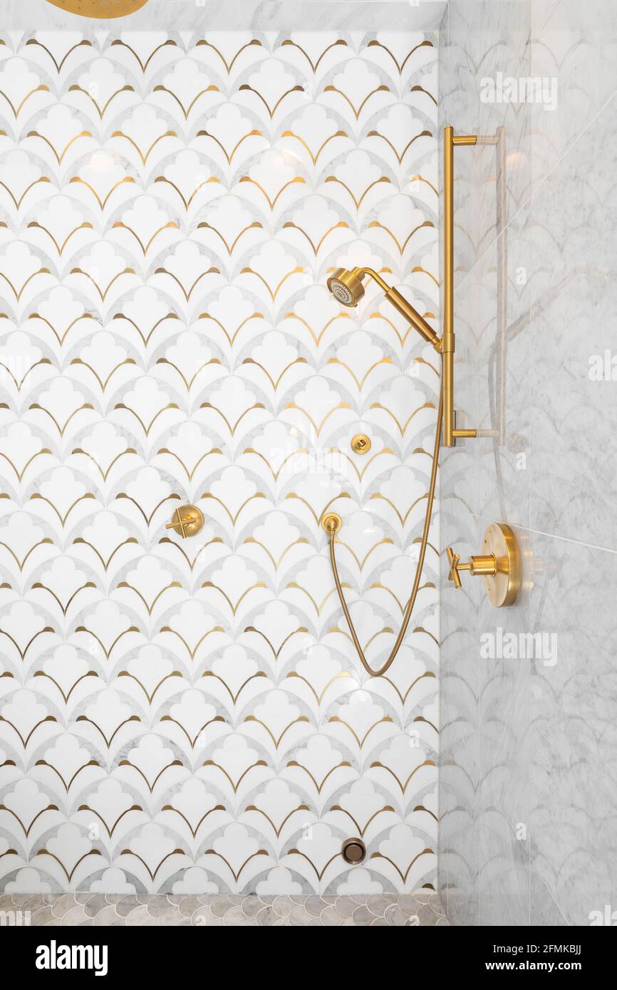 Una bella doccia piastrellata con piastrelle in oro e bianco sulle pareti, piastrelle in marmo a mosaico sul pavimento, soffione doccia in oro e ferramenta. Foto Stock