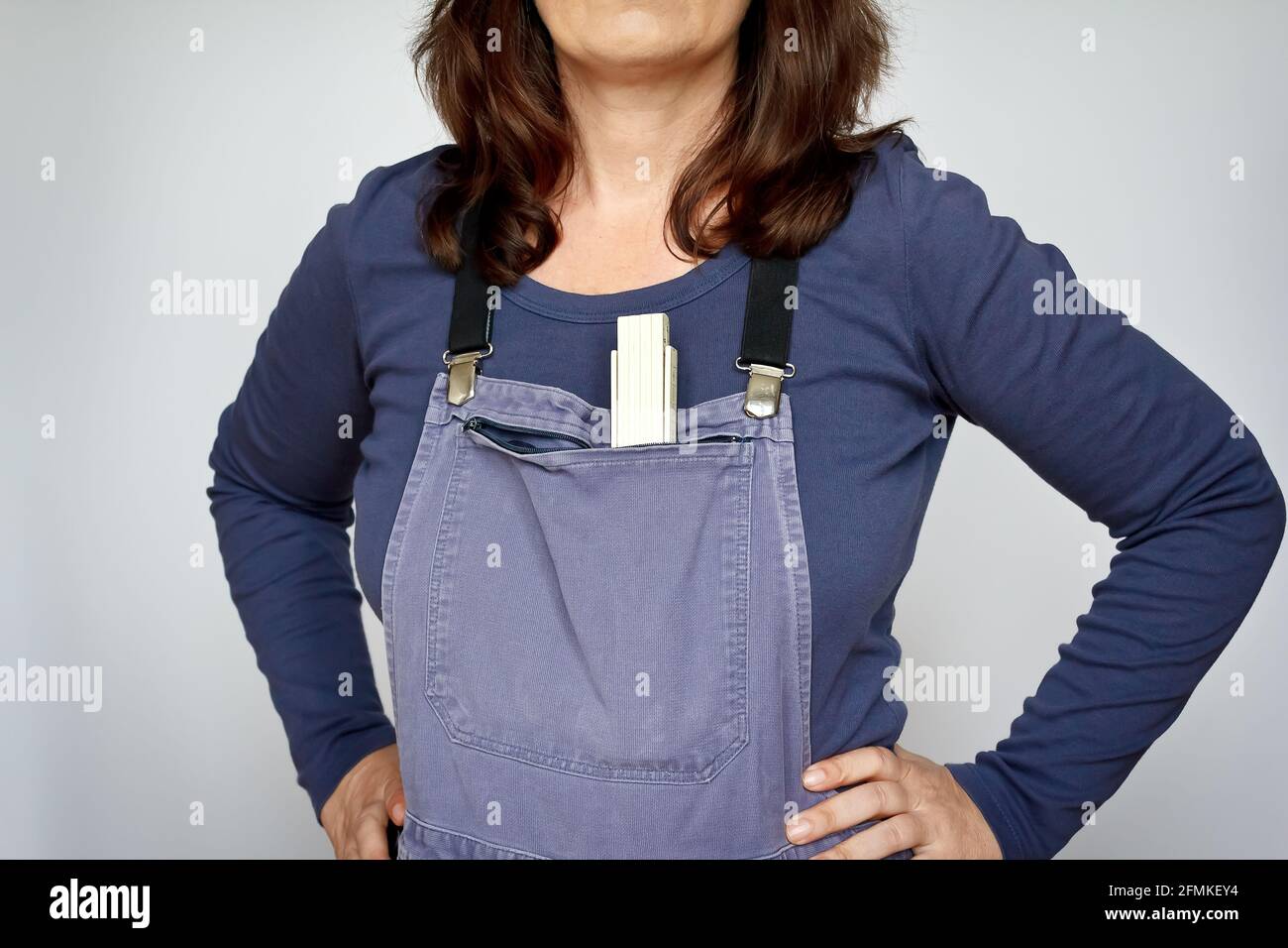 Donna bianca in pantaloni blu di bip o ungarees con un metro, armi akimbo, sfondo chiaro Foto Stock