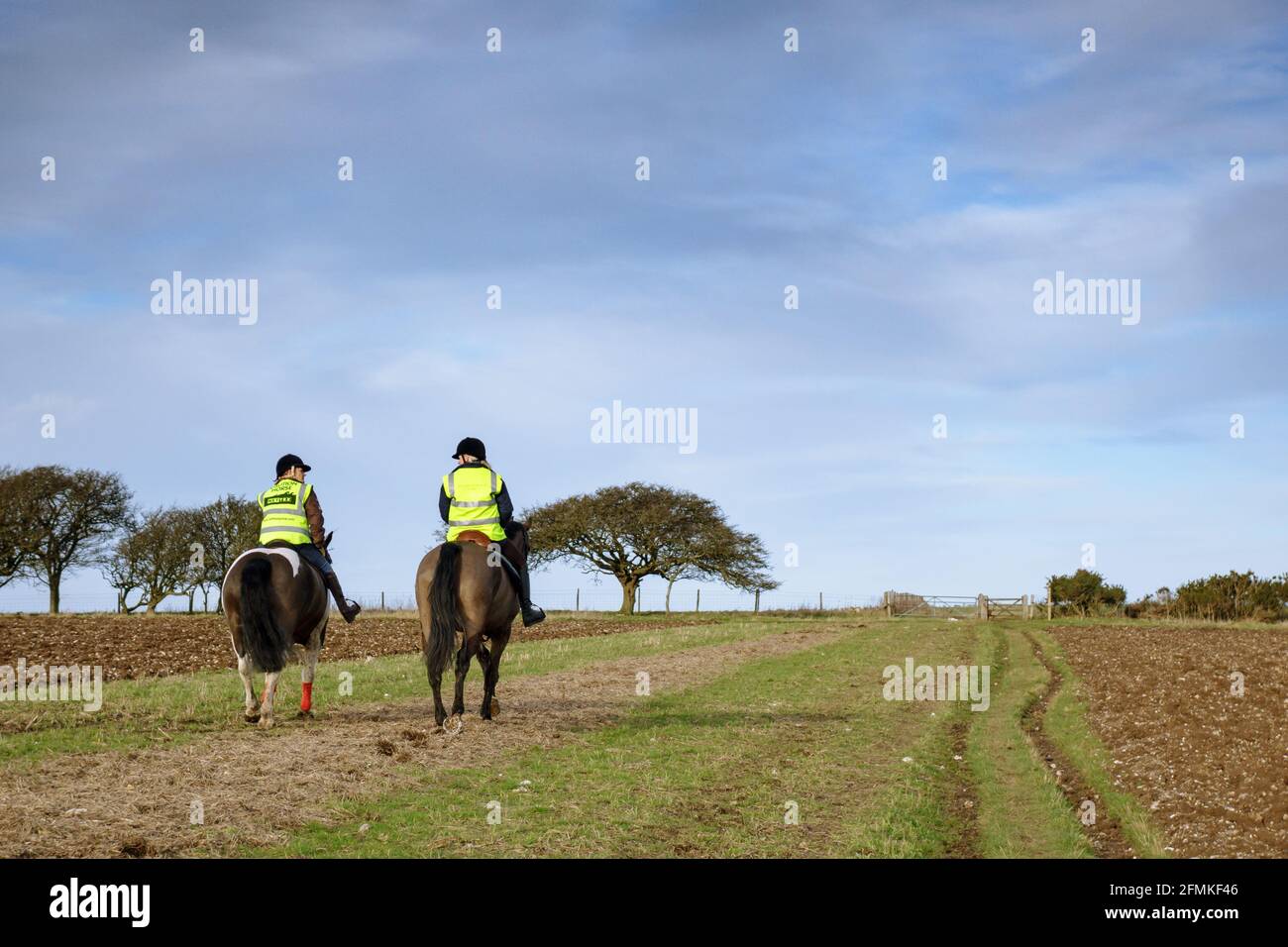 Due donne che cavalcano cavalli indossando giacche ad alta visibilità sul South Downs vicino a Ditchling, Sussex, Inghilterra Foto Stock