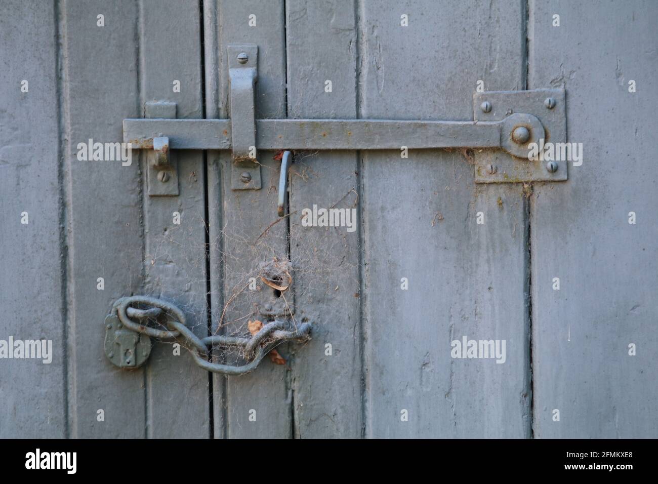 Chiusura della portiera con lucchetto e catena sotto sulla portiera verniciata in legno, ciottoli sopra il foro per chiave. Calke, Derbyshire, Inghilterra, Regno Unito Foto Stock