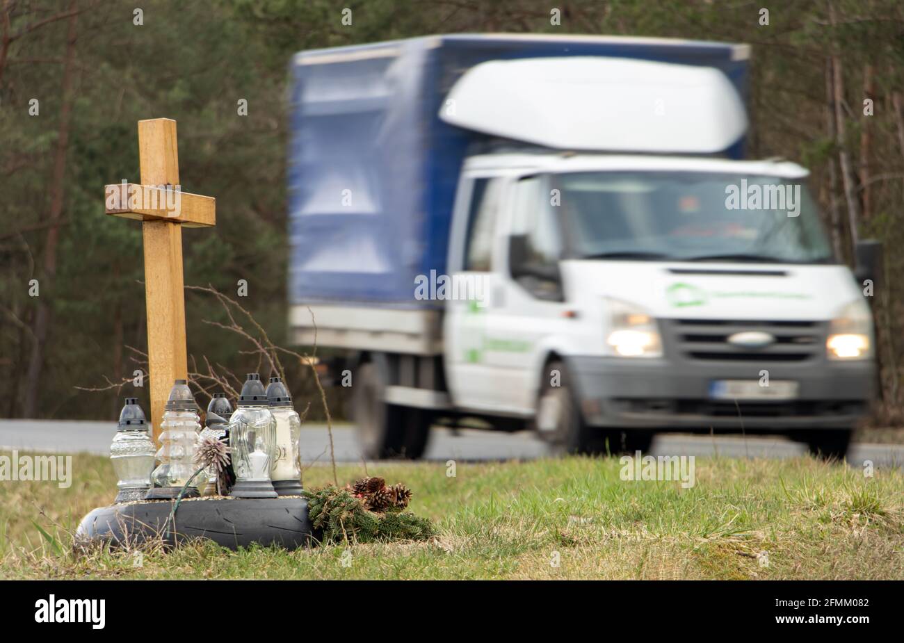 Una croce commemorativa a lato della strada con candele che commemorano la tragica morte, su un percorso di sfondo camion offuscato Foto Stock