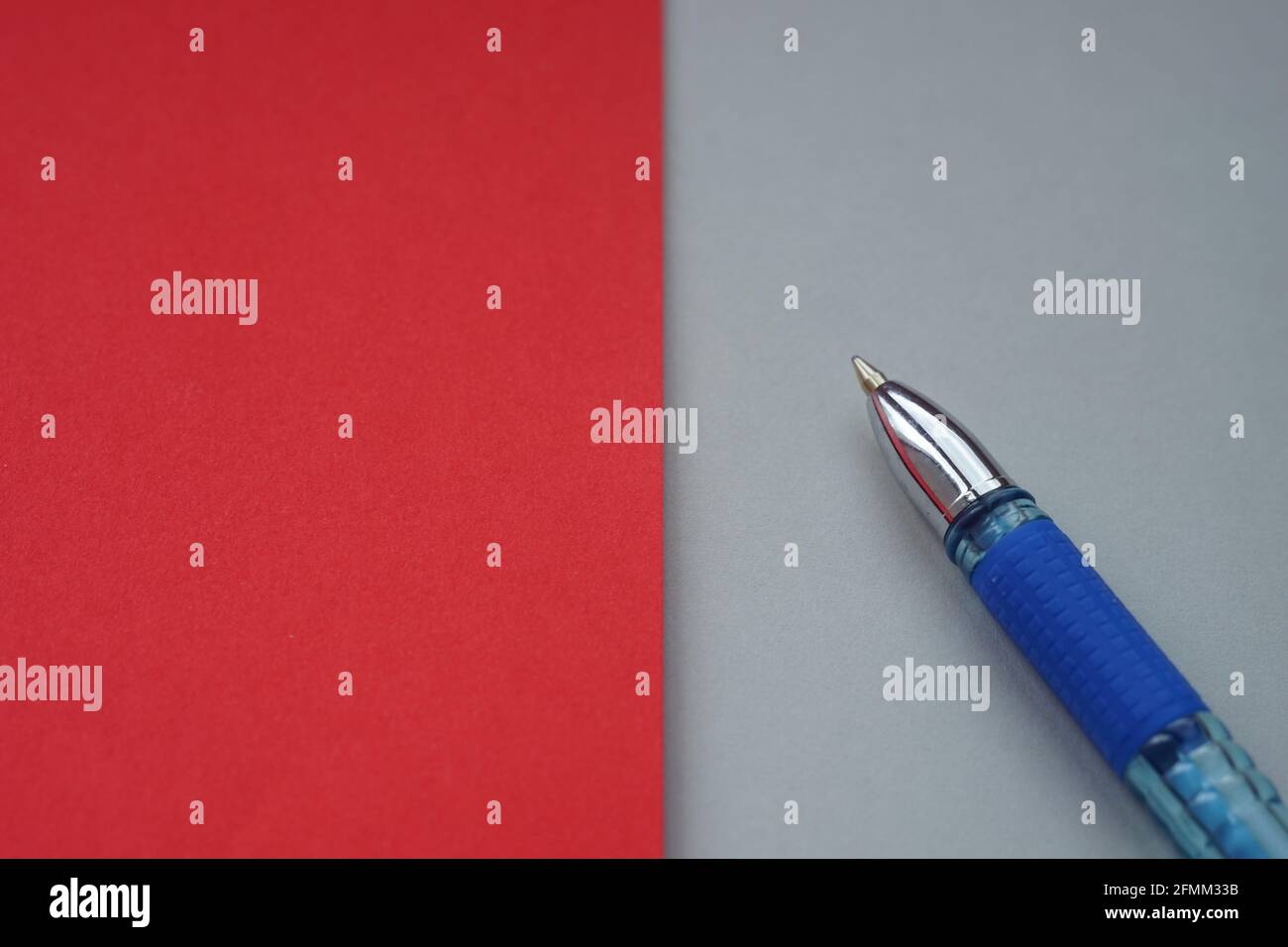 Penna blu a sfera su grigio con carta rossa, spazio per la copia sul lato rosso Foto Stock
