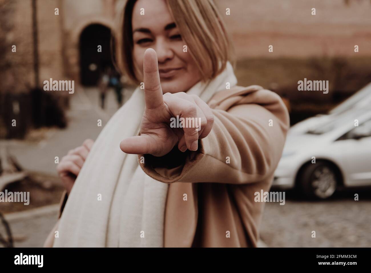 Donna sorridente felice. Una sola donna che flirta e si inarchia un occhio, puntando il dito verso l'alto, fuoco selettivo sul dito, fotografia sfocata, rumore della pellicola Foto Stock