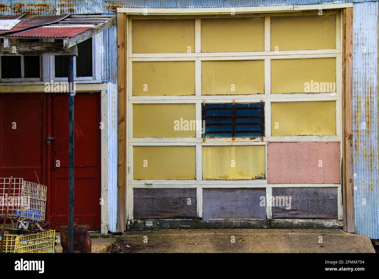 vecchio magazzino abbandonato costruzione struttura garage porta con rosa giallo i colori delle evidenziazioni rosso e blu sono sbiaditi nel tempo scena architettonica rurale Foto Stock