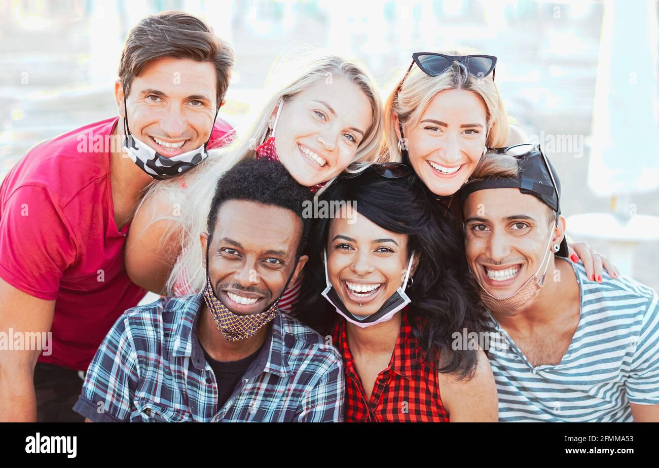 Gruppo di amici multirazziali che scattano una foto mentre si mette a fuoco la fotocamera e sorridono con la maschera facciale - nuovo concetto di stile di vita Foto Stock