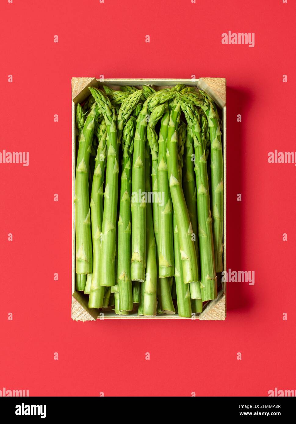 Vista dall'alto con una cassa di legno piena di asparagi verdi crudi su un tavolo rosso. Scatola con asparagi freschi isolati su sfondo rosso. Foto Stock