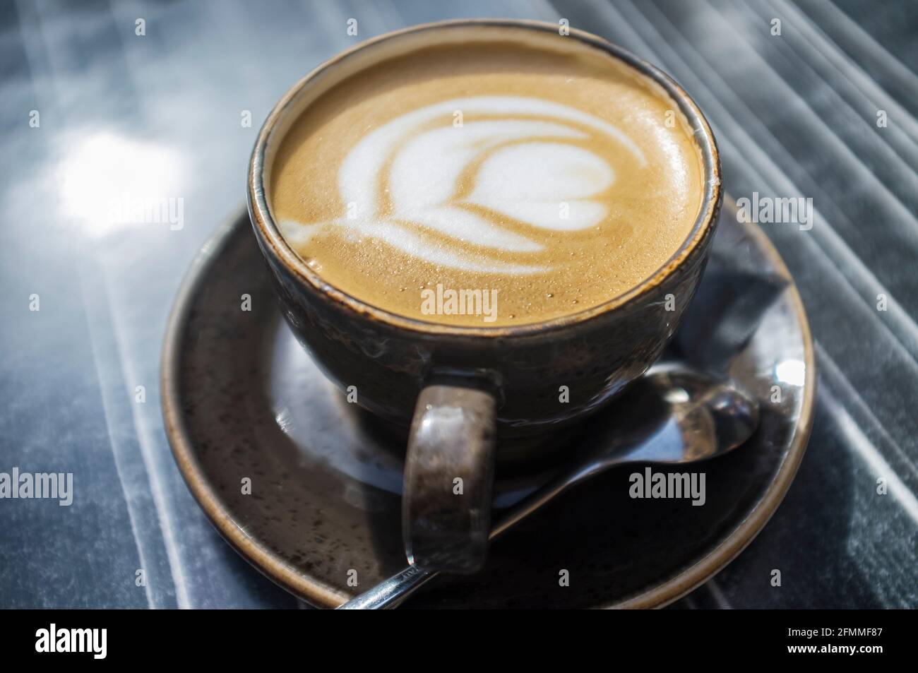 Tazza di caffè fresco con disegno floreale in schiuma. Tavolo di legno scuro come sfondo Foto Stock