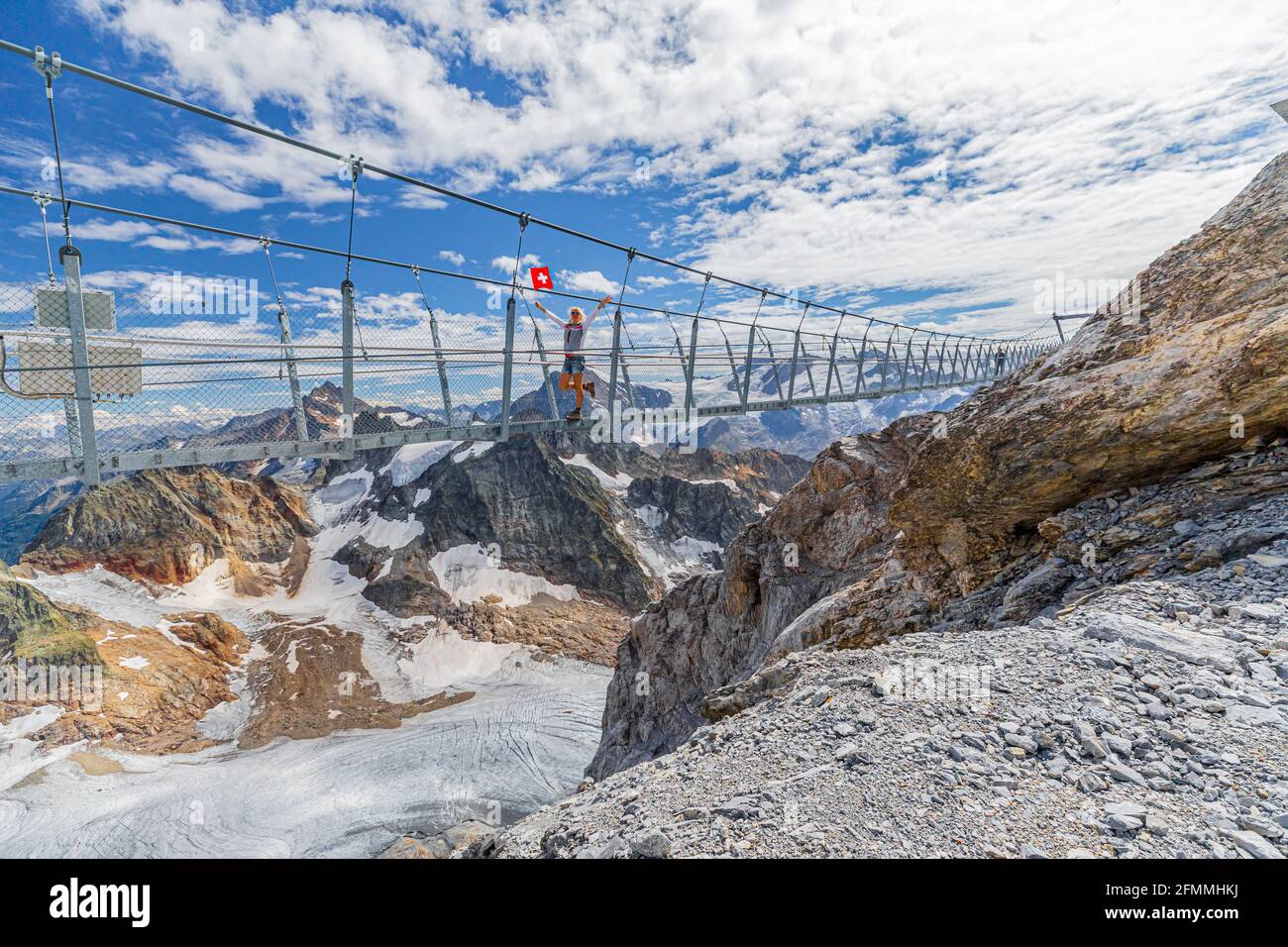 Donna sul ponte sospeso che sventolava una bandiera svizzera. Passeggiata sulla scogliera di Titlis con ghiacciaio nelle Alpi Uri. Punto panoramico a 3028 metri nella stagione estiva, Canton Berna Foto Stock