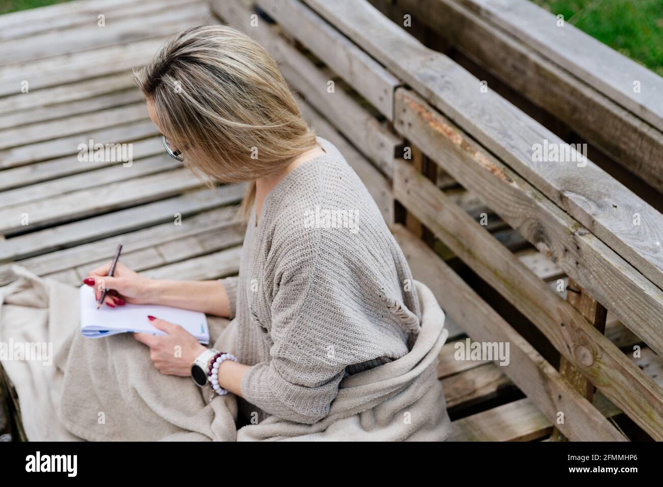 Una donna bionda è seduta, coperta da una coperta, disegnando un disegno o scrivendo un libro. Foto Stock