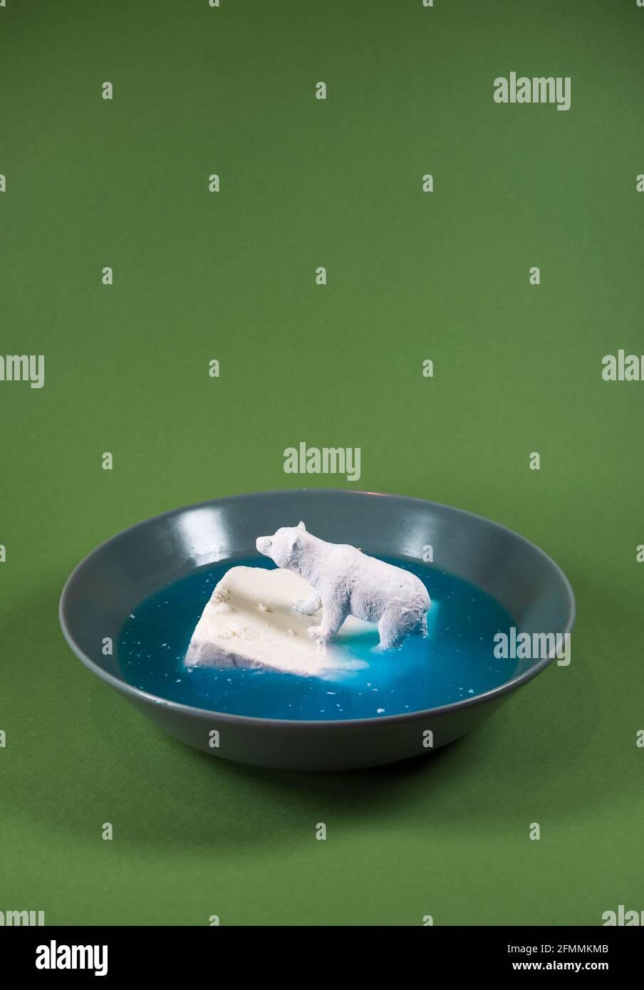 Un piccolo orso polare giocattolo per bambini che galleggia sul formaggio su un piatto in acqua blu. Protezione dell'ambiente, specie in pericolo, habitat naturale e riscaldamento globale. Foto Stock
