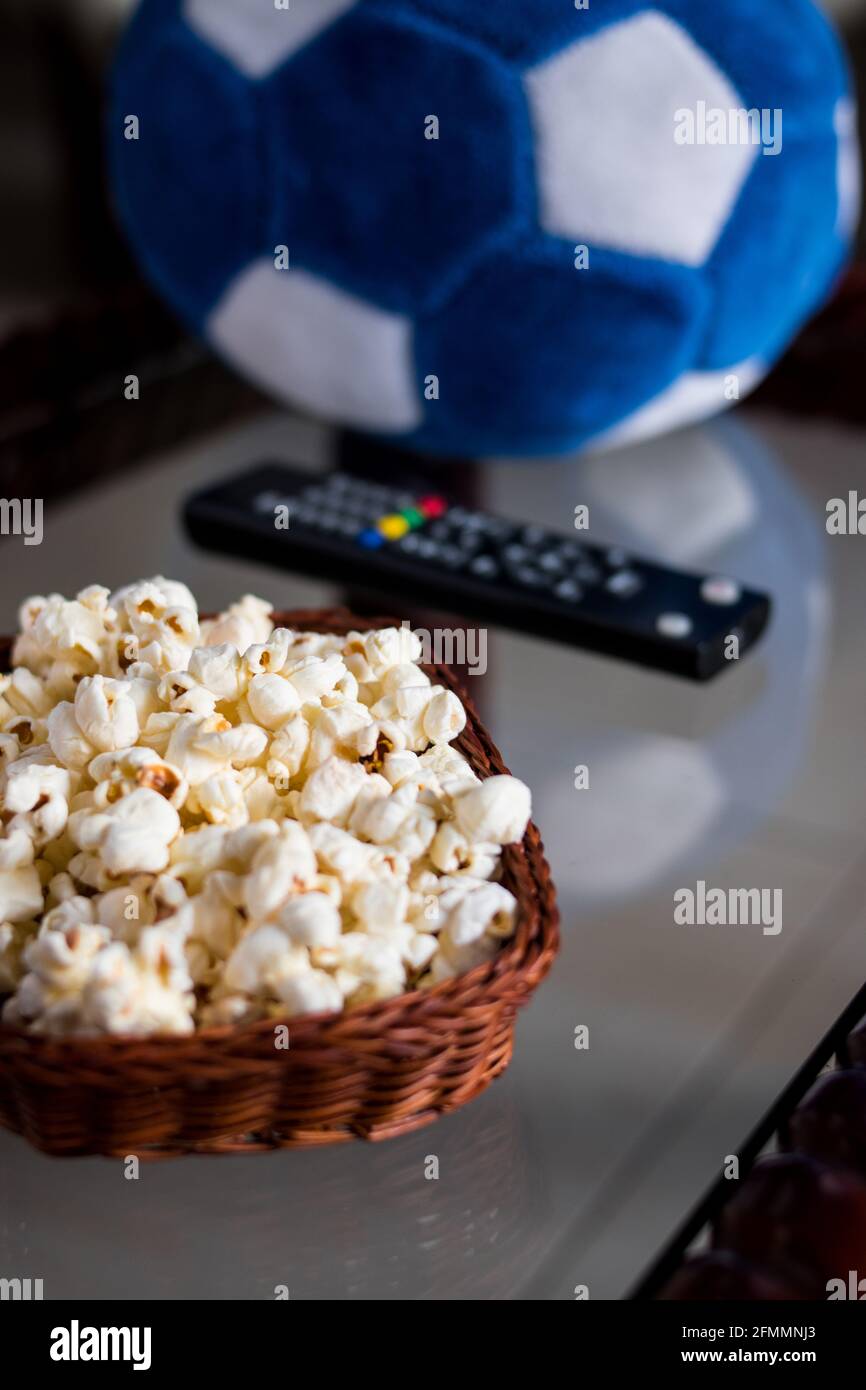 Alcuni pop corn in un cestino con un controllo tv e una palla di calcio su un tavolo a casa Foto Stock