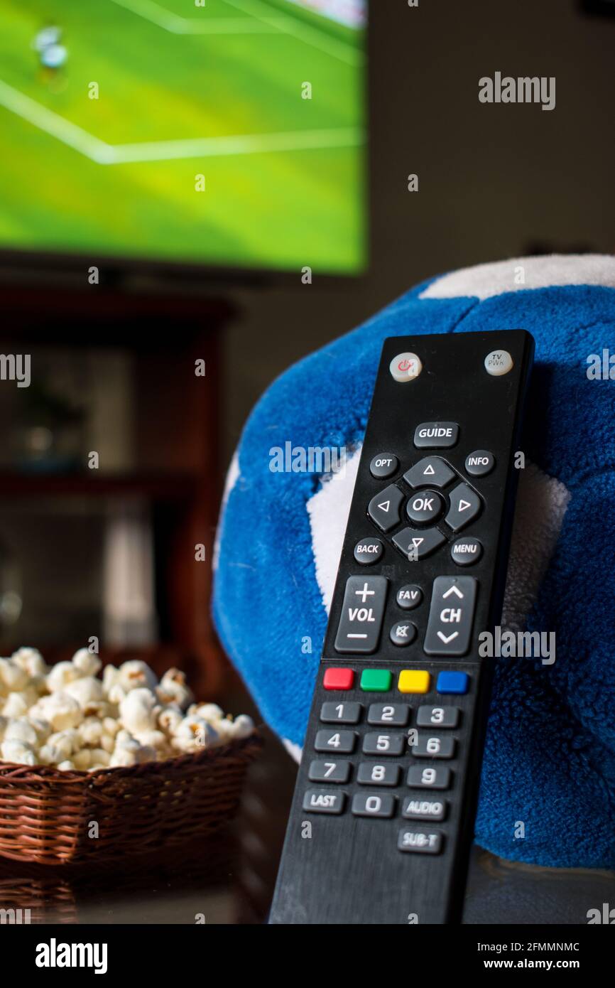 Alcuni pop corn in un cestino con un controllo tv e una palla di calcio su un tavolo a casa Foto Stock