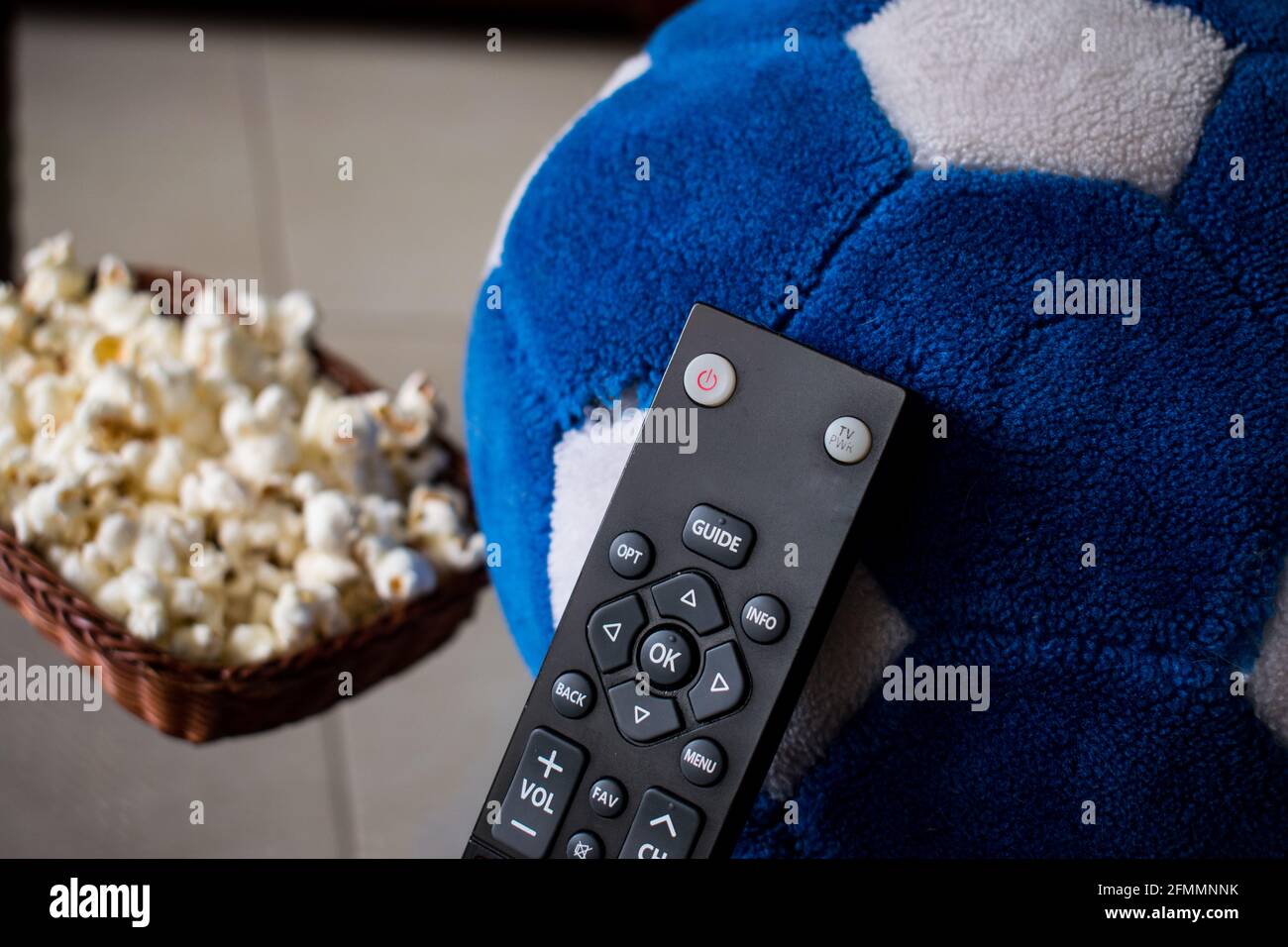 Alcuni pop corn in un cestino con un controllo tv e una palla di calcio su un tavolo a casa Foto Stock