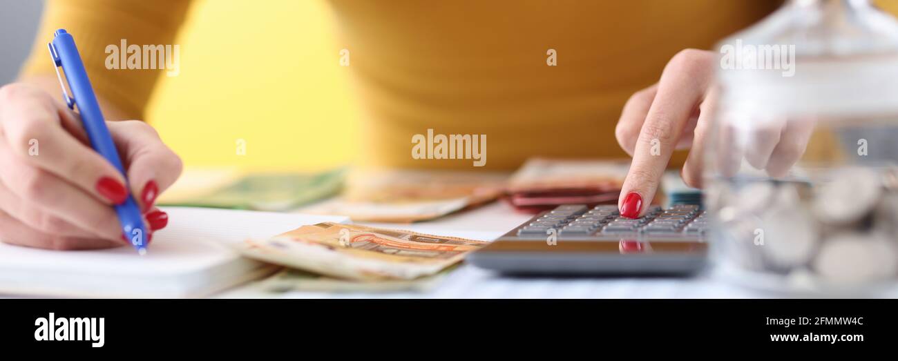 Le mani delle donne tengono la penna e contano le banconote calcolatrice Foto Stock