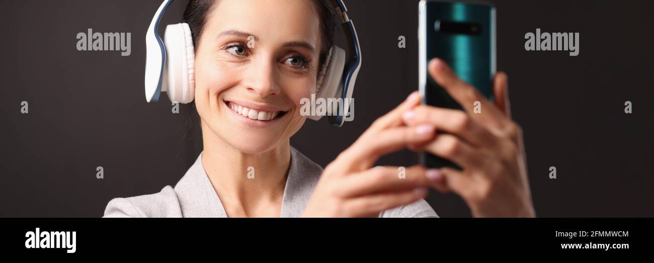 Una donna sorridente con le cuffie guarda allo smartphone Foto Stock