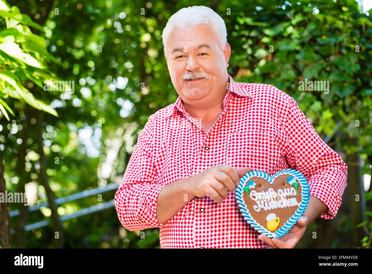 Senior in tradizionali bavaresi vestiti o tracht con lederhosen e panpepato cuore di souvenir in beergarden su Oktoberfest Foto Stock